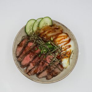 Top view of a savory beef bowl with poached egg and fresh vegetables, perfect for a delicious meal.