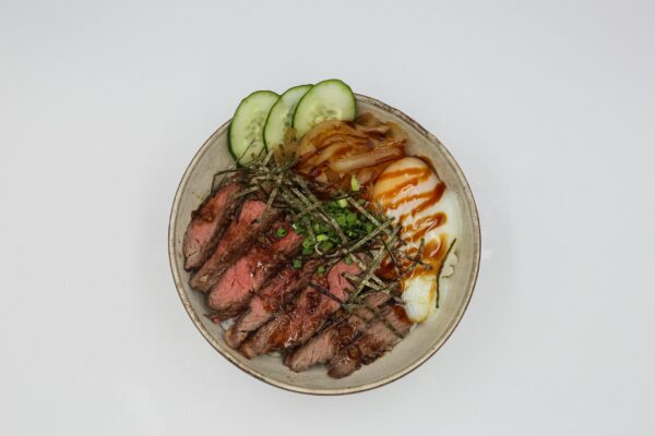 Top view of a savory beef bowl with poached egg and fresh vegetables, perfect for a delicious meal.